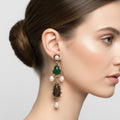 Close-up of an earring with a green gemstone and pearl drops on a person's ear.