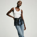 Woman wearing a white tank top and denim skirt with fringe details on a plain background