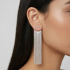 Silver fringe earring worn by a model on a neutral background