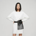 Woman wearing a white dress with a black fringed belt on a gray background