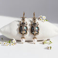 Pair of ornate earrings with gemstones and pearls on a white background