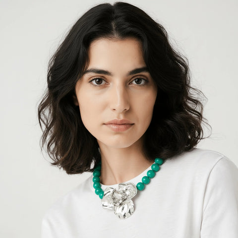 Woman wearing a white top and green beaded necklace with a large silver pendant on a light gray background