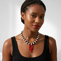 Woman wearing a black and white beaded necklace with a red pendant on a plain background