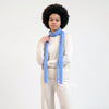 A model with an afro hairstyle wearing a cream-colored knit sweater and matching pants, styled with a light blue knit scarf against a plain white studio background.