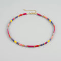 A beaded choker necklace with small rectangular beads in pink, yellow, purple, and red, accented with gold spacer beads and a gold chain extender, shown on a light gray background.