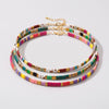 A set of three multi-strand beaded chokers with gold-tone chain extensions, featuring a vibrant mix of colorful square beads and a small white skull bead, displayed on a light gray background.