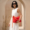 Woman holding a red handbag with braided details in a sunlit archway.