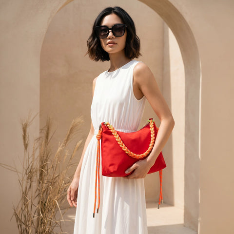Woman holding a red handbag with braided details in a sunlit archway.
