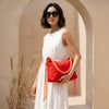 Woman holding a red handbag with braided details in a sunlit archway.