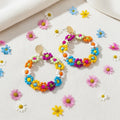 Colorful beaded hoop earrings on a white surface with small flowers around them.