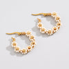 A pair of gold hoop earrings decorated with small white seed beads arranged in a daisy pattern, displayed on a light gray background.