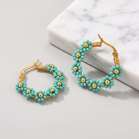 Gold hoop earrings with turquoise flower beads, displayed on a light gray surface next to a white marble block.