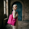 Woman holding a pink tote bag with a unique eye design in a stone building setting.
