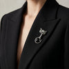 Person wearing a black blazer with a decorative brooch on a neutral background