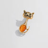 Gold cat-shaped brooch with an orange center on a light gray background