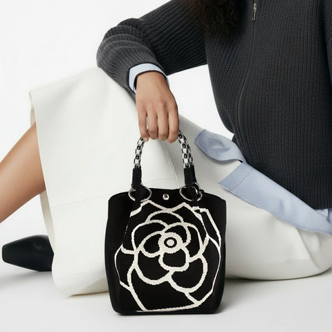 Person holding a black handbag with a white floral design on a white background