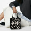 Person holding a black handbag with a white floral design on a white background
