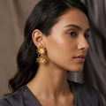 Woman wearing gold floral earrings against a neutral background