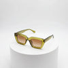 Green sunglasses with brown gradient lenses on a white pedestal against a white background
