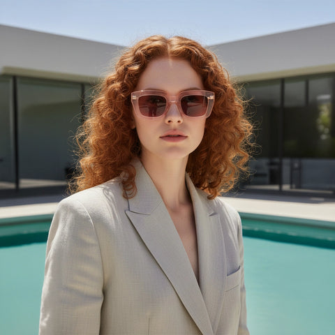 Woman with red hair wearing sunglasses and a beige blazer by a pool.