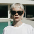 Person wearing sunglasses and a white shirt with a blurred background