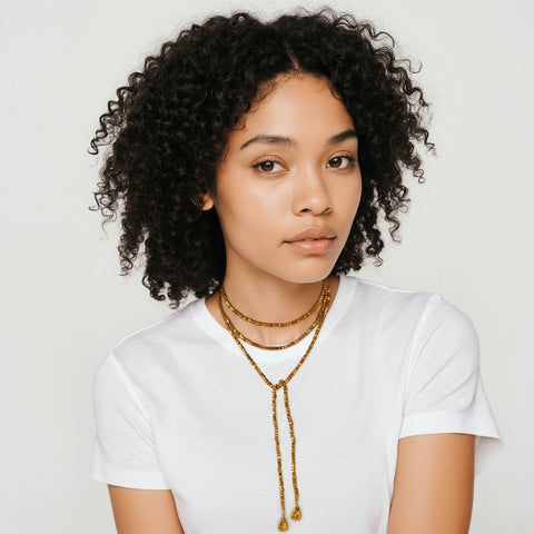 Woman wearing a white t-shirt and gold necklace against a plain background