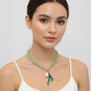 Woman wearing a green necklace with a pendant on a plain background