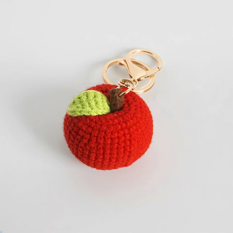 Crocheted red apple keychain with a gold ring on a light gray background
