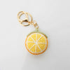 Crocheted lemon keychain with a gold ring on a light gray background