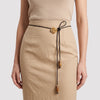 A beige textured midi skirt with a black drawstring waist featuring a gold rose-shaped metal accent and wooden beads, shown on a model.