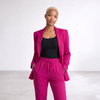 A model wearing a bright magenta pink two-piece pantsuit consisting of a blazer and matching drawstring trousers, styled with a black tank top, against a clean white studio background.