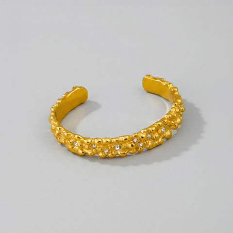Gold bracelet with textured design and small stones on a light gray background