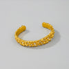 Gold bracelet with textured design and small stones on a light gray background