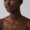 Woman wearing a gold necklace with a pendant on a neutral background