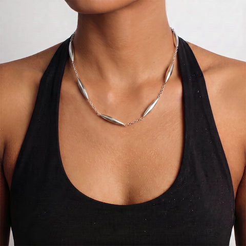 A close-up of a model wearing a silver-toned geometric necklace with elongated teardrop-shaped links over a black halter top.