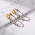 A pair of gold and silver drop earrings with a teardrop-shaped gold top, connected by silver rings and chains, displayed on a white marble slab over a white marble surface.