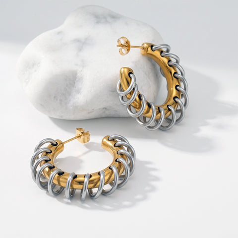 Gold-tone hoop earrings wrapped with silver ring accents, displayed on a white surface beside a marble stone.