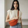 Woman holding an orange quilted bag against a neutral background