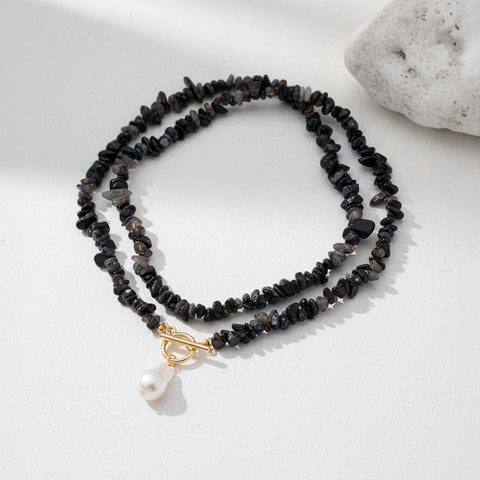 Black beaded necklace with a gold clasp and pearl pendant on a white surface.