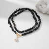 Black beaded necklace with a gold clasp and pearl pendant on a white surface.