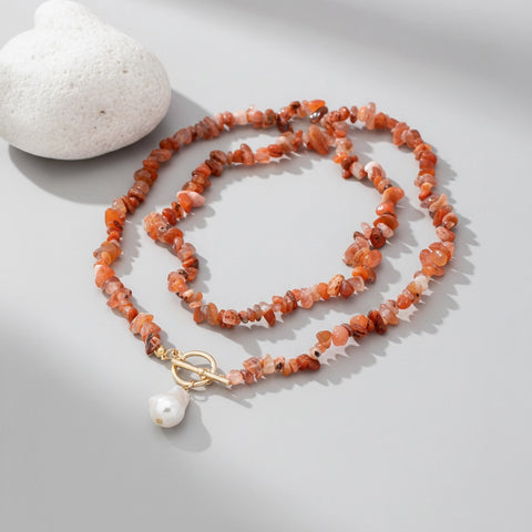 Necklace with orange beads and a gold clasp on a light gray background