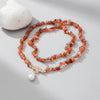 Necklace with orange beads and a gold clasp on a light gray background