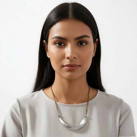Woman wearing a light gray top and a necklace against a white background