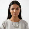 Woman wearing a light gray top and a necklace against a white background