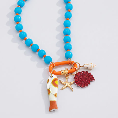 A colorful beaded necklace with bright turquoise blue and orange beads, featuring a gold-tone ring clasp and three dangling charms: a white and orange fish-shaped charm, a gold starfish, and a textured red flower.