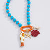 A colorful beaded necklace with bright turquoise blue and orange beads, featuring a gold-tone ring clasp and three dangling charms: a white and orange fish-shaped charm, a gold starfish, and a textured red flower.