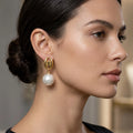 Close-up of a woman wearing gold earrings with pearls against a neutral background