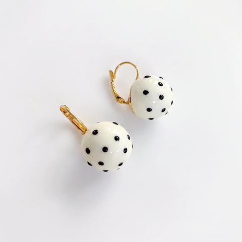 A pair of gold hoop earrings with white spherical beads decorated with black polka dots, shown on a clean white background.