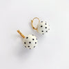 A pair of gold hoop earrings with white spherical beads decorated with black polka dots, shown on a clean white background.