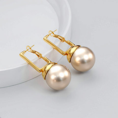 Gold earrings with large pearls on a light gray background